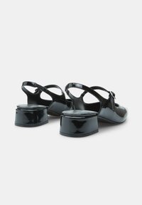 Črne lakirane usnjene čevlje s slingback obliko in zaobljenim nosom, majhnim blokastim petkom ter z plastiko na trakcu. Gladka, sijoča tekstura.