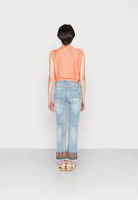 Oranssi hihaton paita, vaaleansiniset leveälahkeiset farkut brodeeratulla helmalla ja litteät sandaalit. Siistit linjat, pehmeä materiaali ja rento muotoilu.