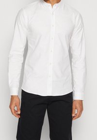 Witte lange mouwen shirt met een Mandarin kraag, met knoopsluiting en een gladde textuur, gecombineerd met donkere broek.