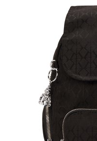 Sac à dos en tissu noir avec un motif géométrique, poche avant zippée, fermeture à rabat et un charm en métal argenté en forme de robot accroché.