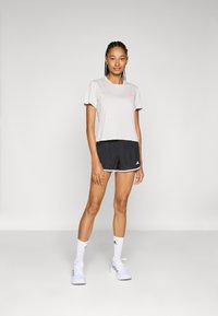 Világosszürke cropped póló rózsaszín logóval, fekete shorts fehér részletekkel, fehér sportzsák és világos színű cipők. Egyszerű dizájn.