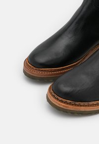 Schwarze Lederstiefel mit runden Zehen, braun genähtem Leder-Welt und durchsichtigen Gummisohlen auf einem weißen Hintergrund.