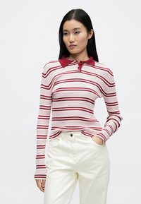 Ribstrikket langærmet polo i lyserød med mørkerøde striber og krave; har en tre-knaps stolpe og let udvidede ærmer.