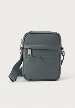 Bolsa transversal de couro cinza com superfície texturizada, bolso frontal com zíper e logótipo da marca em relevo. Inclui uma alça ajustável e ferragens metálicas.