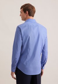 Niebieska koszula w długim rękawie z klasycznym kołnierzem, subtelnym wzorem w kropki i zapinanymi mankietami. Dopasowany krój z zaokrąglonym dołem z tyłu.