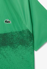 Grön kortärmad skjorta med gradientmönster från ljus till mörk, med en liten logotyp i det övre vänstra hörnet. Tillverkad av ett mjukt tyg.