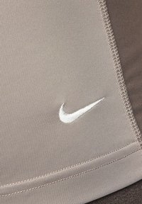 Nike urheilusukat vaaleassa taupe-kankaassa, jossa on ribbejä. Siinä on valkoinen brodeerattu logo ja litteät saumat mukavuutta varten.