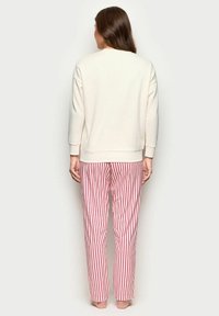 Felpa crema con maniche lunghe abbinata a pantaloni da pigiama a righe rosse e bianche. Il tessuto sembra morbido con una vestibilità comoda.