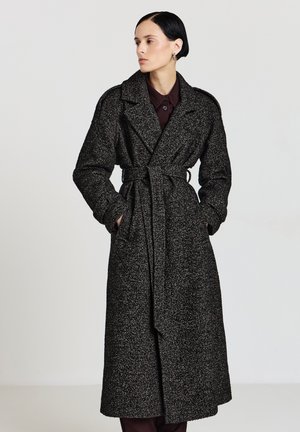 Lungo cappotto bianco e nero con motivo a fantasia, vita con cintura, ampi risvolti e tessuto strutturato. Presenta maniche lunghe e taglio dritto.