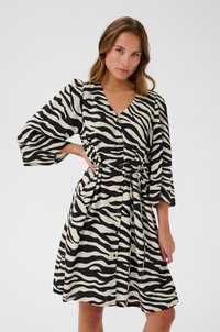 Robe à rayures zèbre noire et crème avec un décolleté en V, des manches trois-quarts, des boutons sur le devant et une taille nouée. Texture de tissu lisse.
