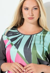 Monivärinen pusero, jossa on sinivihreä ja vaaleanpunainen abstrakti kuvio, mustat hihat, sileä pinta ja pyöreä pääntie.