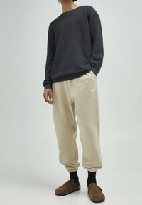 Czarny teksturowany sweter z długimi rękawami, w połączeniu z beżowymi zwężanymi spodniami dresowymi z małym logo. Dopełnieniem stroju są brązowe buty wsuwane.