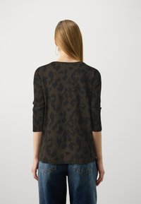 Maglietta a maniche lunghe di colore verde scuro con motivo a macchie di leopardo nere. Presenta un collo rotondo e una vestibilità rilassata, abbinata a jeans azzurri chiari.