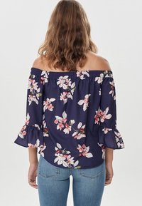 Navy sininen off-the-shoulder-paita kukkakuviolla, rypytetyllä kaula-aukolla ja levenevillä hihoilla. Pehmeä kangas, kevyt ja rento muotoilu.