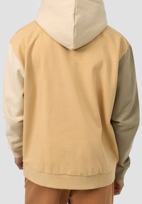 Huvtröja med en beige och ljusbrun färgblockdesign, med en avslappnad passform och strukturerad tyg. Ribbad ärm- och fållkant.