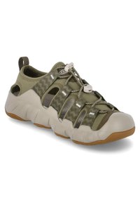 Oliwkowe buty sportowe z oddychającą siateczką, elastycznymi sznurówkami i wyściełaną beżową gumową podeszwą. Posiada boczne wycięcia i uchwyt do zakupu.