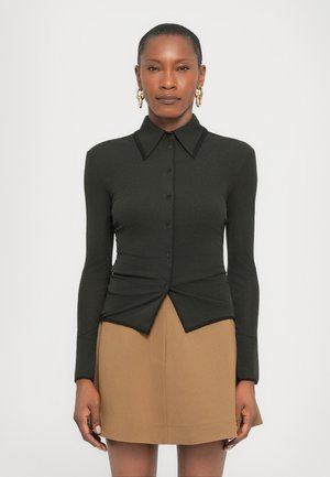 Black long-sleeve shirt with a pointed collar, button closure, and twisted front design; paired with a tan skirt. Smooth texture, fitted style.