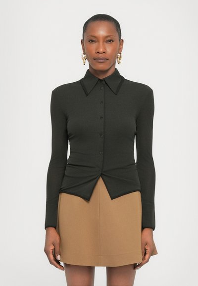 Schwarzes Langarmshirt mit spitzem Kragen, Knopfverschluss und verdrehtem Design vorne; kombiniert mit einem tanfarbenen Rock. Glatte Textur, figurbetonter Schnitt.