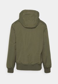 Chaqueta con capucha de color verde oliva, con una textura suave y mate, puños elásticos y un dobladillo ajustado. Sin cierres visibles ni detalles de logo.