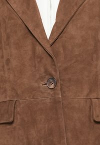 Blazer en suede marron avec col cranté, fermeture par un bouton unique et deux poches avant. Texture lisse avec une finition douce et mate.