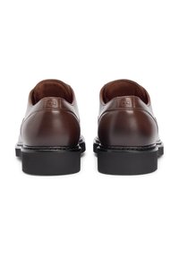 Καφέ δερμάτινα παπούτσια με λεία υφή, χαμηλό προφίλ και μαύρες λαστιχένιες σόλες. Διαθέτουν διακριτική επωνυμία στο πίσω μέρος.