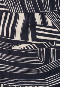 Tissu avec un motif de lignes géométriques noir et blanc comprenant une petite étiquette cousue portant la mention "Street One" sur une poche.