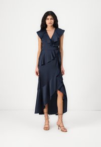 Vestido de marinheiro com mangas em babados, saia em camadas, fenda alta e cintura ajustada. Combinado com saltos de tiras bejes.
