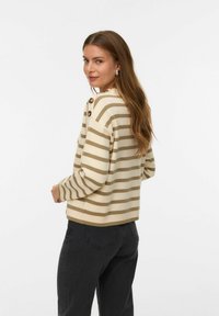 Pull en beige à rayures avec un col rond, accents de boutons sur l'épaule, coupe décontractée, associé à un jean foncé, texture de tissu lisse.