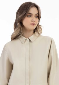 Beige læderjakke med en knap-op krave og frontplade. Har en glat tekstur, diskret syninger og en afslappet pasform.