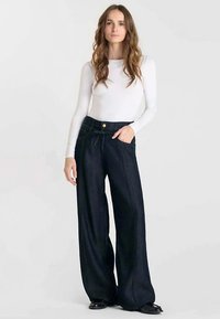 Wijde, donker denim broek met hoge taille, voorzakken en een gebonden ceintuur. De stof heeft een gladde afwerking met subtiele textuurdetails.