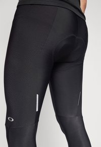 Schwarze Radshorts mit strukturierten Einsätzen, die einen enganliegenden Schnitt haben, reflektierende Akzente und Logodetails aufweisen. Technisches, dehnbares Material.