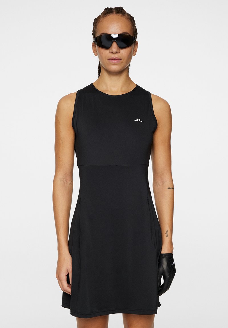 Robe de sport noire à design sans manches, col rond, poches latérales et logo sur la poitrine. Tissu mat avec coupe et texture sportives.