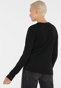 Schwarzes Langarmshirt aus weichem Material, mit rundem Halsausschnitt und figurbetontem Design. Die Rückseite zeigt eine einfache, nahtlose Optik.