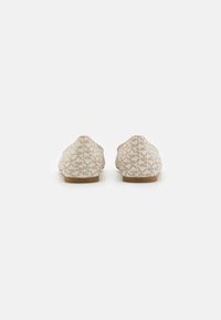 Beige flache Schuhe mit einem diskreten geometrischen Muster auf dem Stoff, von hinten auf einer weißen Oberfläche betrachtet.
