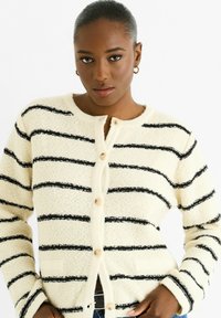 Cream fuzzy cardigan with black horizontal stripes, round neckline, four buttons down the front, and two side pockets.