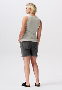 Grå ärmlös topp, figurnära design, kombinerad med grå denimshorts. Svarta sandaler. Bakifrån framhäver vy bilden av plaggets släta textur och form.