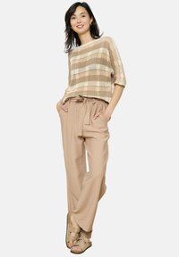 Bežs adīts cropped tops ar rūtainu rakstu, apvienots ar brīvām bežām biksēm ar elastīgu jostu un sasietu detaļu.