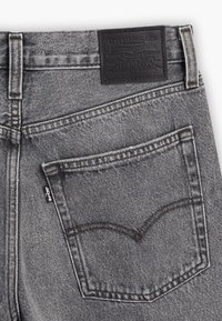 Poche arrière d'un jean Levi's gris délavé avec une étiquette de marque en cuir noir et une petite étiquette en tissu Levi's.
