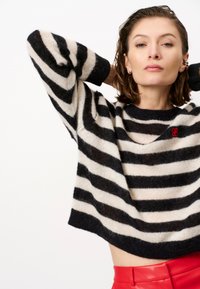 Zwart en crèmekleurig gestreept sweater met een losse pasvorm en geribbelde manchetten, met een klein rood logo aan de voorkant en een cropped ontwerp.