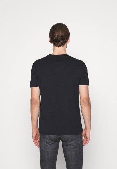 Short-sleeve black t-shirt in soft fabric, round neck, fitted cut, with a smooth texture. Worn by a person facing away against a light background.
