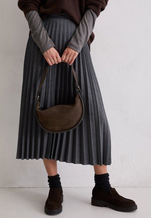 Grauer Faltenrock mit hoher Taille, braune Wildledertasche in geschwungener Form, dunkle Socken und braune Slipper mit dicker Sohle.