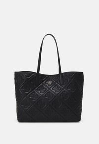 Sac cabas matelassé noir avec anses d'épaule, motif embossé et petite plaque métallique avec le logo indiquant GUESS EST 1981 au centre devant.