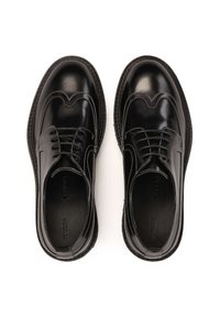 Zapatos de cuero negro pulido con detalles de brogue, cierre de cordones, costuras en contraste blancas y una suela de goma texturizada.