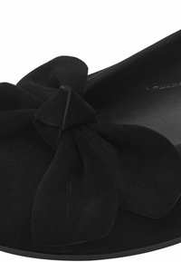 Chaussure plate en suede noir avec un accent de nœud prononcé à l'avant, intérieur lisse et forme arrondie.