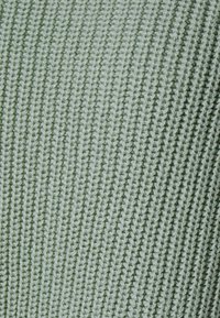 Gros plan d'un tissu tricoté vert clair montrant un motif de point côtelé vertical et une texture de fil doux.