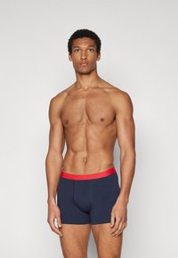 Herren Navy-Boxershorts mit rotem Bund, aus Baumwollmaterial, enganliegendem Schnitt und ohne sichtbare Muster oder Grafiken. Glatte Textur.