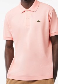 T-shirt à manches courtes, en rose corail, avec un col côtelé, une Patte de boutonnage à trois boutons et un petit logo vert sur la poitrine gauche.
