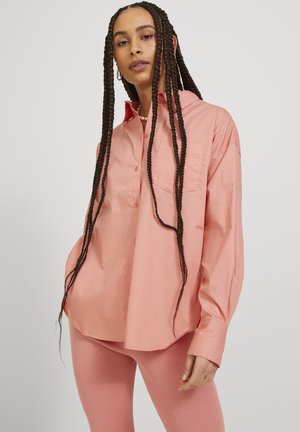 Överdimensionerad långärmad skjorta i mjuk rosa tyg med spetsig krage, framficka och knäppning, i kombination med ribbade rosa leggings.