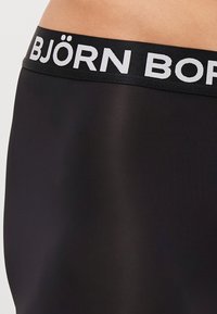 Schwarze Stoffunterwäsche mit einer glatten Textur und einem breiten Gummibund, auf dem in weißen Buchstaben "BJÖRN BORN" gedruckt ist.