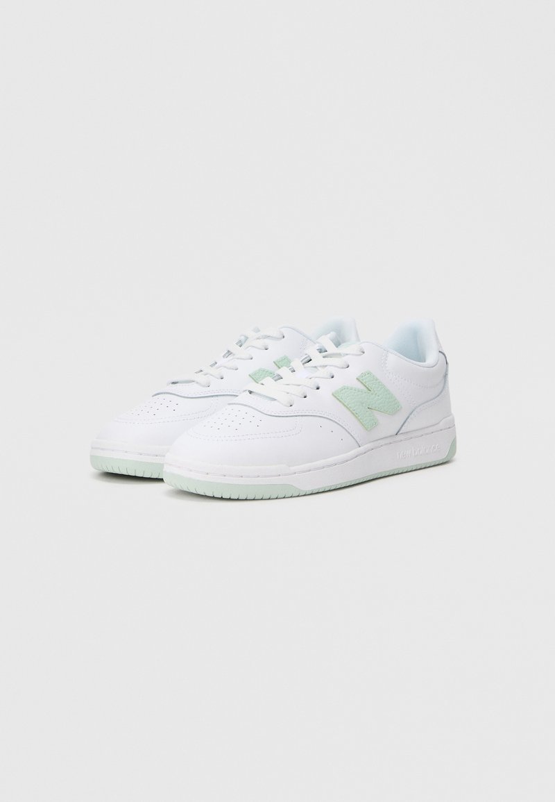 Zapatillas blancas con acentos en verde claro, parte superior de cuero, puntera perforada, cordones redondos y una suela texturizada con un sutil detalle de marca.